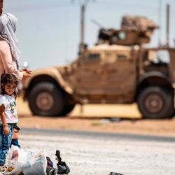 Una familia se encuentra frente a un vehículo militar estadounidense estacionado en las afueras de Rumaylan en la provincia de Hasakeh, en el noreste de Siria, controlada por los kurdos. | Foto:DELIL SOULEIMAN / AFP