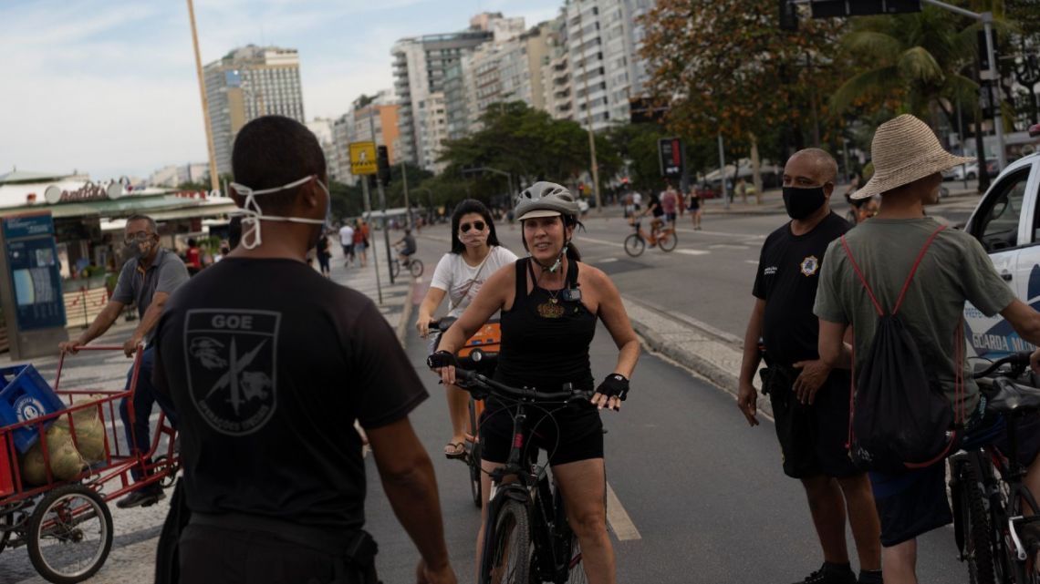 A municipal guard stops a woman on a bike to tell her to wear a mask at Copacabana beach amid the outbreak of the new coronavirus in Rio de Janeiro, Brazil, Sunday, July 12, 2020.