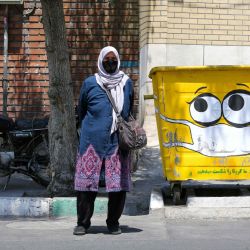 Una mujer iraní se para al lado de un cubo de la calle, pintada con el dibujo de una máscara en una campaña para dar a conocer la pandemia de coronavirus COVID-19, en un barrio del sur de la capital Teherán. | Foto:TTA KENARE / AFP