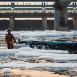Un hombre tira un bote en medio de la espuma en el río Yamuna contaminado en las afueras de Nueva Delhi. | Foto: Xavier Galiana / AFP