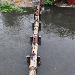 La gente camina a través de una tubería de agua elevada sobre un canal de aguas residuales inundado después de una lluvia monzónica en Nueva Delhi. | Foto:Sajjad Hussain / AFP