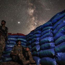 Esta fotografía de larga exposición muestra la galaxia de la Vía Láctea elevándose en el cielo sobre los combatientes sirios del grupo del Frente Nacional para la Liberación respaldado por Turquía mientras está de guardia entre sacos de arena en la ciudad de Taftanaz a lo largo de las líneas del frente en la provincia del noroeste de Idlib, controlada por los rebeldes del país. | Foto:OMAR HAJ KADOUR / AFP