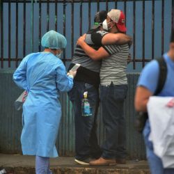 Los familiares de una presunta víctima de COVID-19 se abrazan cerca de trabajadores de la salud en un hospital de campaña. | Foto:ORLANDO SIERRA / AFP