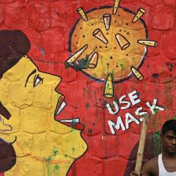 Un trapero se para frente a un mural sobre la conciencia del coronavirus COVID-19, pintado en una pared a lo largo de la carretera en Nueva Delhi. | Foto:SAJJAD HUSSAIN / AFP