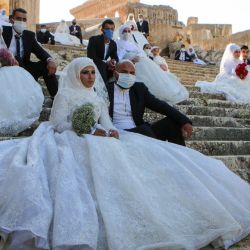 Las parejas libanesas, con máscaras protectoras, se sientan en los escalones durante una boda grupal en el Templo de Baco en el sitio histórico de Baalbek en el valle oriental de Bekaa en Líbano. | Foto:AFP