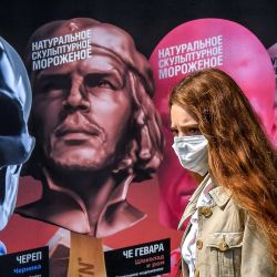 Una mujer con una máscara facial para protegerse contra la enfermedad por coronavirus pasa junto a un póster publicitario en Moscú. | Foto:YURI KADOBNOV / AFP