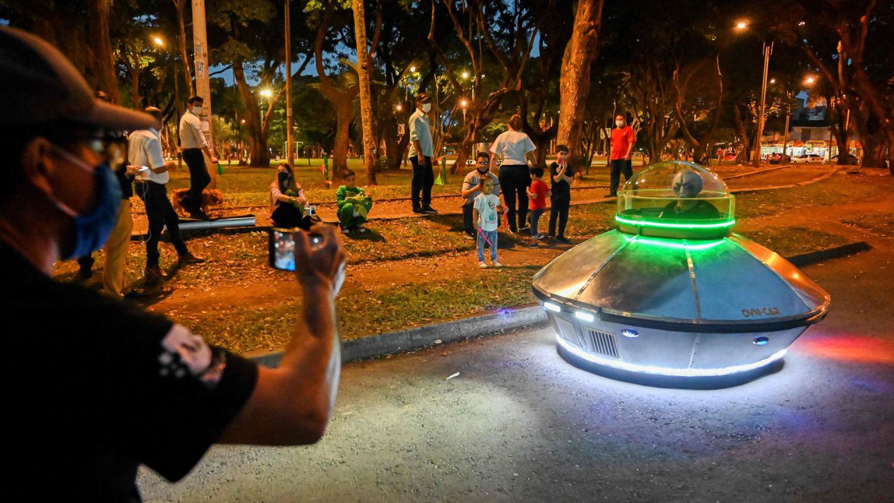 Un hombre toma una foto de un hombre enmascarado que viajaba en un automóvil de juguete con forma de ovni en un parque en Cali, Colombia, antes de que comience el toque de queda nocturno contra la propagación del nuevo coronavirus. | Foto:Luis Robayo / AFP