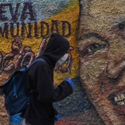 Un hombre con máscaras y guantes protectores pasa junto a un mural que representa al fallecido presidente de Venezuela, Hugo Chávez, en el barrio de La Vega en Caracas. | Foto:Federico Parra / AFP