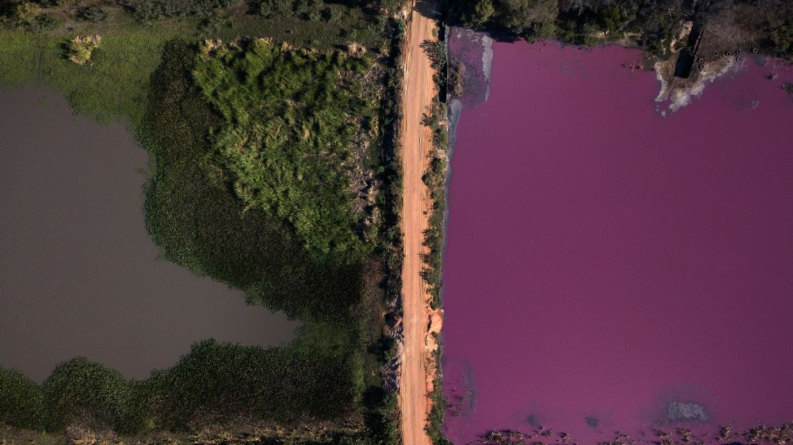 A road divides the Cerro Lagoon, where the water at right is colored and the Waltrading S.A. tannery stands on the bank, top right, in Limpio, Paraguay, Wednesday, Aug. 5, 2020. According to Francisco Ferreira, a technician at the National University Multidisciplinary Lab. who is taking water samples at the site on Wednesday, the color of the water is due to the presence of heavy metals like chromium, commonly used in the tannery process.