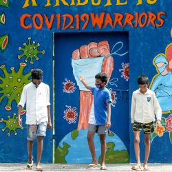 Un joven hace un gesto mientras camina con otros frente a un mural dedicado a los trabajadores de primera línea que luchan contra la propagación del coronavirus COVID-19, en Chennai. | Foto:Arun Sankar / AFP