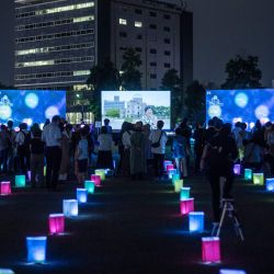 Los visitantes miran una pantalla (parte posterior C) que muestra linternas virtuales mientras se colocan linternas de papel para conmemorar el 75 aniversario del bombardeo atómico, en un parque en Hiroshima. | Foto:Philip Fong / AFP