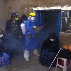 Un empleado funerario con equipo de protección desinfecta la casa de una víctima de COVID-19 mientras los familiares lloran afuera, antes de llevar el ataúd al cementerio local para su entierro en el remoto pueblo aymara de Acora, en las tierras altas, a una hora de la ciudad de Puno, cerca de la frontera con Bolivia. | Foto:Carlos Mamani / AFP)