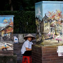Un vendedor espera a los clientes sentado detrás de los gabinetes de electricidad decorados con pinturas a lo largo de una calle en Hanoi. | Foto:MANAN VATSYAYANA / AFP
