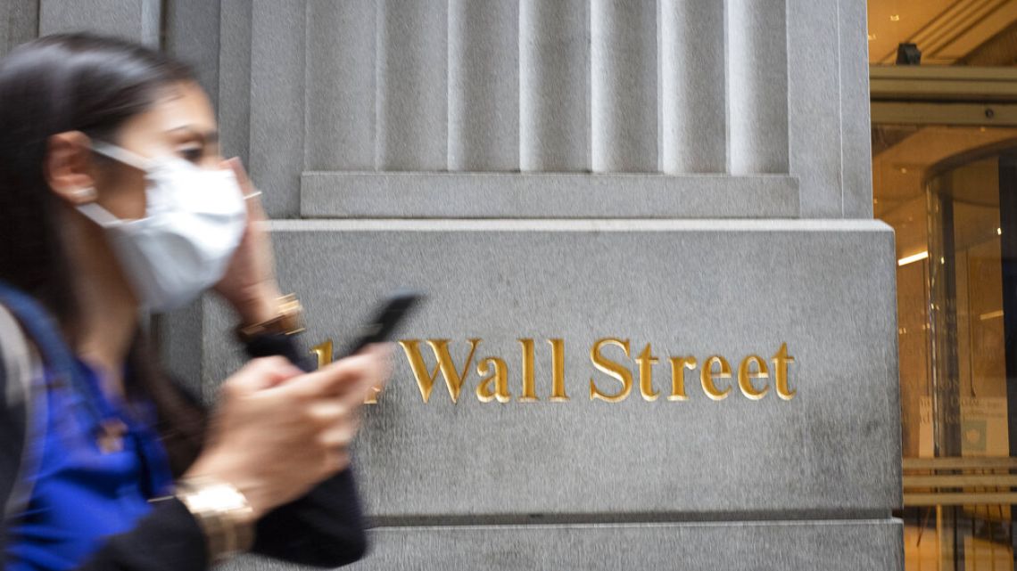 A woman wearing a mask passes a sign for Wall Street during the coronavirus pandemic. Stocks are opening higher on Wall Street, pushing the S&P 500 ever closer to the all-time high it reached back in February, before the coronavirus shutdowns slammed the economy. The index was up 0.3% in the early going Tuesday, Aug. 11. 