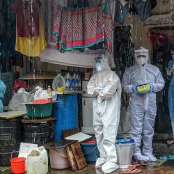Los trabajadores de la salud que usan trajes de equipo de protección personal (EPP) se refugian mientras realizan una prueba de detección del coronavirus COVID-19 bajo una lluvia intensa en Mumbai. | Foto:INDRANIL MUKHERJEE / AFP