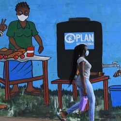 Una mujer con mascarilla pasa junto a un grafiti que promueve el lavado de manos y el uso de mascarillas como medidas preventivas contra la propagación del coronavirus COVID-19, en Kibera, Nairobi. | Foto:Simon Maina / AFP