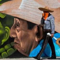 Un mariachi pasa junto a un graffiti en Mérida, estado de Yucatán, México, en medio de la pandemia del coronavirus COVID-19. | Foto:HUGO BORGES / AFP