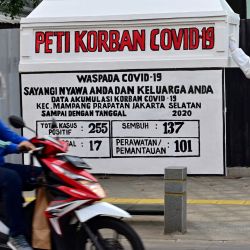 Un motociclista pasa junto a una instalación que muestra un ataúd, un maniquí con equipo de protección personal y un tablero que muestra las estadísticas de infección por coronavirus COVID-19 para el área, en Yakarta. | Foto:ADEK BERRY / AFP