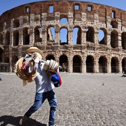 Un vendedor ambulante lleva sombreros de paja y gorras fuera del monumento del Coliseo en Roma durante la infección por COVID-19, causada por el nuevo coronavirus. | Foto:Vincenzo Pinto / AFP