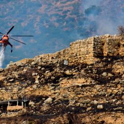 Un helicóptero de extinción de incendios arroja agua para extinguir las llamas durante un incendio forestal cerca del sitio arqueológico de Micenas en el noreste del Peloponeso. | Foto:Eurokinissi / AFP
