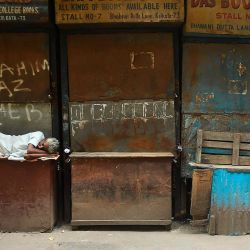 Un hombre descansa frente a los puestos de libros cerrados durante un día de cierre impuesto por el estado como medida preventiva contra el aumento de casos de coronavirus Covid-19, en Calcuta. | Foto:Dibyangshu Sarkar / AFP