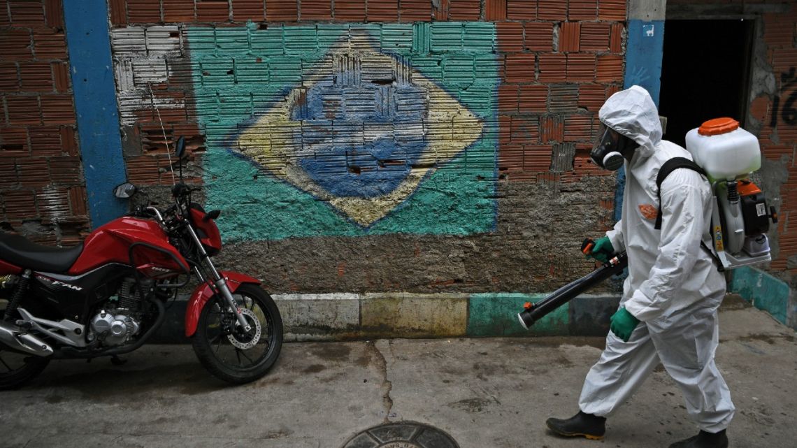 A volunteer wearing PPE walks past a mural depicting a Brazilian flag as he disinfects an area at the Babilonia favela, in Rio de Janeiro, Brazil. Brazil will announce on September 1, 2020 a record economic contraction in the second trimester, which can reach up to 10%, mitigated anyhow by massive aid agreed to face the coronavirus pandemic.  