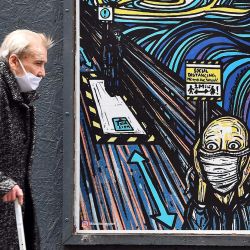 Un peatón anciano que usa una máscara facial o se cubre debido a la pandemia de COVID-19, pasa junto a grafitis que representan a los sujetos dentro de obras de arte famosas, pero con máscaras, en Glasgow. | Foto:Andy Buchanan / AFP