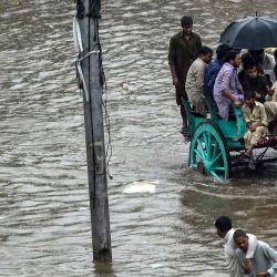 Los hombres montan un carro tirado por caballos en una calle inundada durante las fuertes lluvias monzónicas en Lahore. | Foto:Arif Ali / AFP