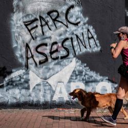 Una mujer pasa corriendo junto a un mural contra el expresidente colombiano (2002-2010) Álvaro Uribe, que fue pintado y ahora muestra un graffiti contra las FARC, una vez el grupo guerrillero más poderoso del continente americano y ahora el partido político reformado de las FARC, en Bogotá. | Foto:Juan Barreto / AFP