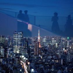 La Torre de Tokio se ilumina entre el horizonte de la ciudad mientras los visitantes se reflejan en el vidrio mientras visitan la plataforma de observación Shibuya Sky en Tokio. | Foto:Philip Fong / AFP