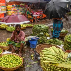 Un vendedor que vende bananas sostiene un paraguas mientras espera a los clientes durante una lluvia monzónica en Dhaka. | Foto:Munir Uz Zaman / AFP