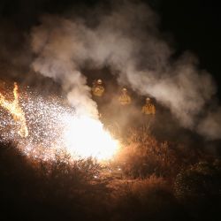 Los bomberos encienden una bengala para provocar un incendio en la espalda mientras trabajan para contener el incendio Bobcat que se quema en una ladera cerca de las casas en Monrovia, California. | Foto:Mario Tama / Getty Images / AFP