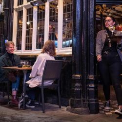 Una camarera lleva bebidas mientras la gente bebe afuera de un pub en Soho, en el centro de Londres. | Foto:Tolga Akmen / AFP