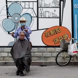 Un peluquero le corta el pelo a un cliente en una calle de Beijing. | Foto:NOEL CELIS / AFP