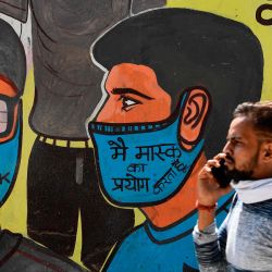 Un hombre pasa junto a un mural que representa a los guerreros de primera línea del coronavirus Covid-19, pintado en la pared de un vertedero en Nueva Delhi. | Foto:Sajjad Hussain / AFP
