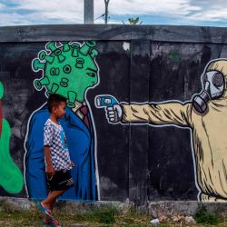 Un niño pasa junto a un mural que representa el coronavirus COVID-19 en Surabaya, Java Oriental. | Foto:JUNI KRISWANTO / AFP