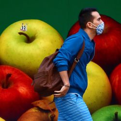 Un hombre que llevaba una mascarilla pasa junto a la pared de un supermercado que muestra una fotografía mural de manzanas en Barcelona. | Foto:LLUIS GENE / AFP