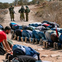 Los soldados israelíes se quedan esperando mientras los manifestantes palestinos realizan las oraciones musulmanas del viernes durante una manifestación contra los asentamientos judíos en la ciudad de Asira Shamaliya en la ocupada Cisjordania cerca de Nablus. | Foto:Abbas Momani / AFP