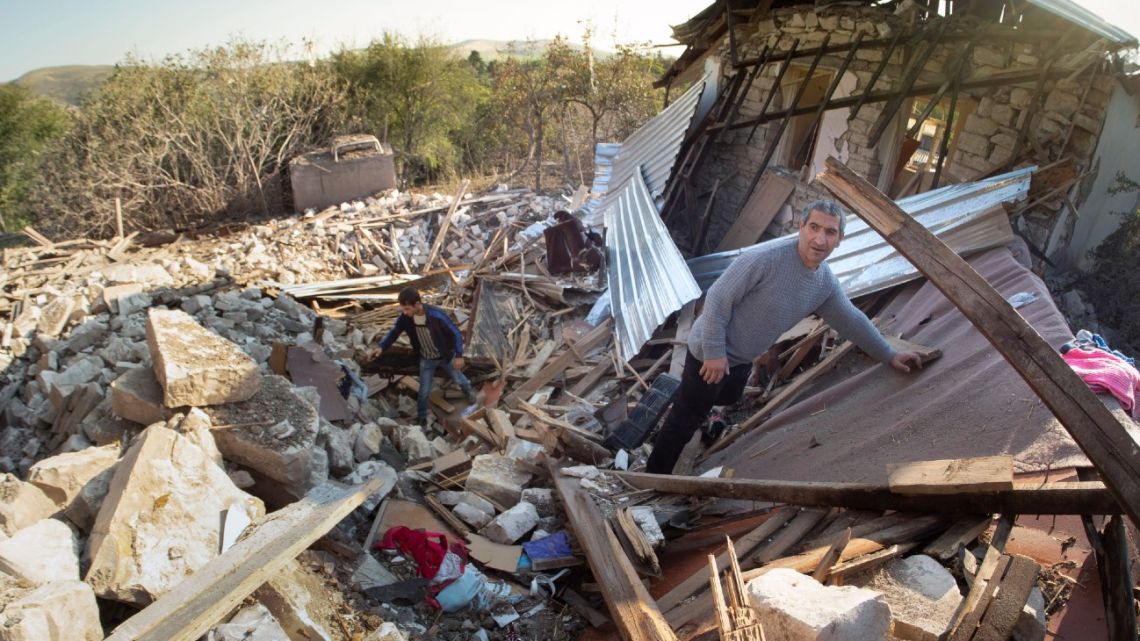 Garik Ovanisyan, right, climbs in a bomb crater at his house destroyed by shelling by Azerbaijan's artillery in the town of Martuni, the separatist region of Nagorno-Karabakh, Wednesday, October 14, 2020.