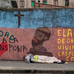 Un indigente duerme en una acera junto a un muro leyendo “El amor de Dios se percibe en las pequeñas cosas” en Montevideo. - Cientos de personas duermen en las calles de Montevideo, capital de un país considerado su paso exitoso por la pandemia, pero que no ha podido escapar del crecimiento de la pobreza en la región más desigual del planeta. Una encuesta del Ministerio de Desarrollo Social muestra que hasta agosto de 2020 había 2553 personas viviendo en la calle, un 25,3% más que en 2019. | Foto:Eitan Abramovich / AFP