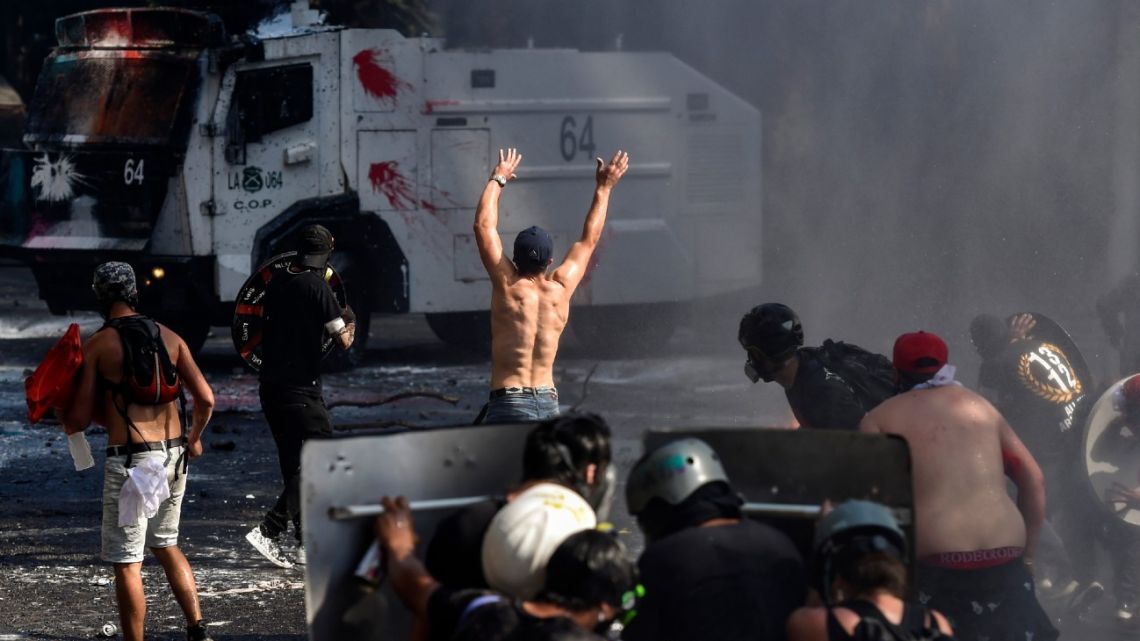 Demonstrators clash with a riot police vehicle during the commemoration of the first anniversary of the social uprising in Chile, in Santiago, on October 18, 2020, as the country prepares for a landmark referendum. Changing the constitution enacted under former dictator Augusto Pinochet, who ruled from 1973-90, was a key demand of protesters during the two months of violent civil unrest against the government and inequality. Chileans will be asked two questions on October 25: do they want a new constitution and who should draft it. 