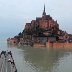 La fotografía aérea muestra una carretera parcialmente cubierta de agua desde donde la gente mira el Mont-Saint-Michel, en Normandía, noroeste de Francia, rodeada por el mar durante la marea alta. - Desde 1979, el sitio del Mont Saint-Michel y su bahía es un sitio del patrimonio mundial de la UNESCO. | Foto:Damien Meyer / AFP