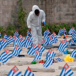 Un trabajador municipal con traje de bioseguridad porta flores entregadas previamente por un familiar de una víctima de COVID-19, para ser depositadas en su tumba en el cementerio La Bermeja durante el Día de Muertos en San Salvador. | Foto:Yuri Cortez / AFP