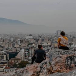 Los turistas se sientan en la colina Aeropagus con vistas a la niebla de Atenas mientras los cafés, bares y restaurantes cierran debido a un cierre parcial para detener la propagación del Covid-19. | Foto:Louisa Gouliamaki / AFP