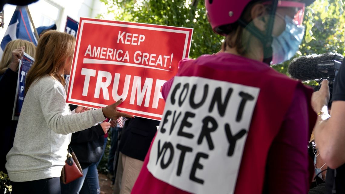 A Trump supporter holds a campaign sign at a rally during the 2020 Presidential election outside the Republican National Committee headquarters in Washington DC.