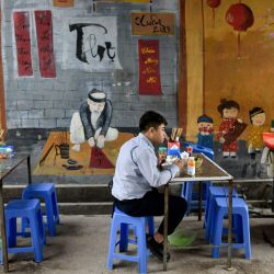 Un hombre almuerza en un puesto de comida al lado de la calle en Hanoi. | Foto:Manan Vatsyayana / AFP