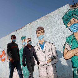 Hombres palestinos pasan junto al arte callejero que muestra a los médicos con máscaras debido a la pandemia del coronavirus COVID-19, en Khan Yunis, en el sur de la Franja de Gaza. | Foto:Mohammed Abed / AFP