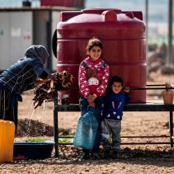 Una mujer y niños sirios, desplazados de Ras al-Ain, una ciudad fronteriza controlada por Turquía y sus representantes sirios, usan agua de un tanque en el campamento de Washokani en la gobernación de al-Hasakeh en el noreste de Siria. | Foto:Delil Souleiman / AFP