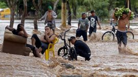 Una pèrsona carga plátanos mientras camina cerca de hombres sentados en una calle inundada en El Progreso, departamento de Yoro, Honduras, luego del paso del huracán Iota, ahora degradado a tormenta tropical.