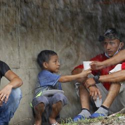 Un niño come junto a los hombres mientras se refugian bajo el puente de La Democracia mientras esperan que los familiares sean rescatados por miembros de la marina de las inundaciones provocadas por el paso del huracán Iota en El Progreso, departamento de Yoro, Honduras. | Foto:STR / AFP